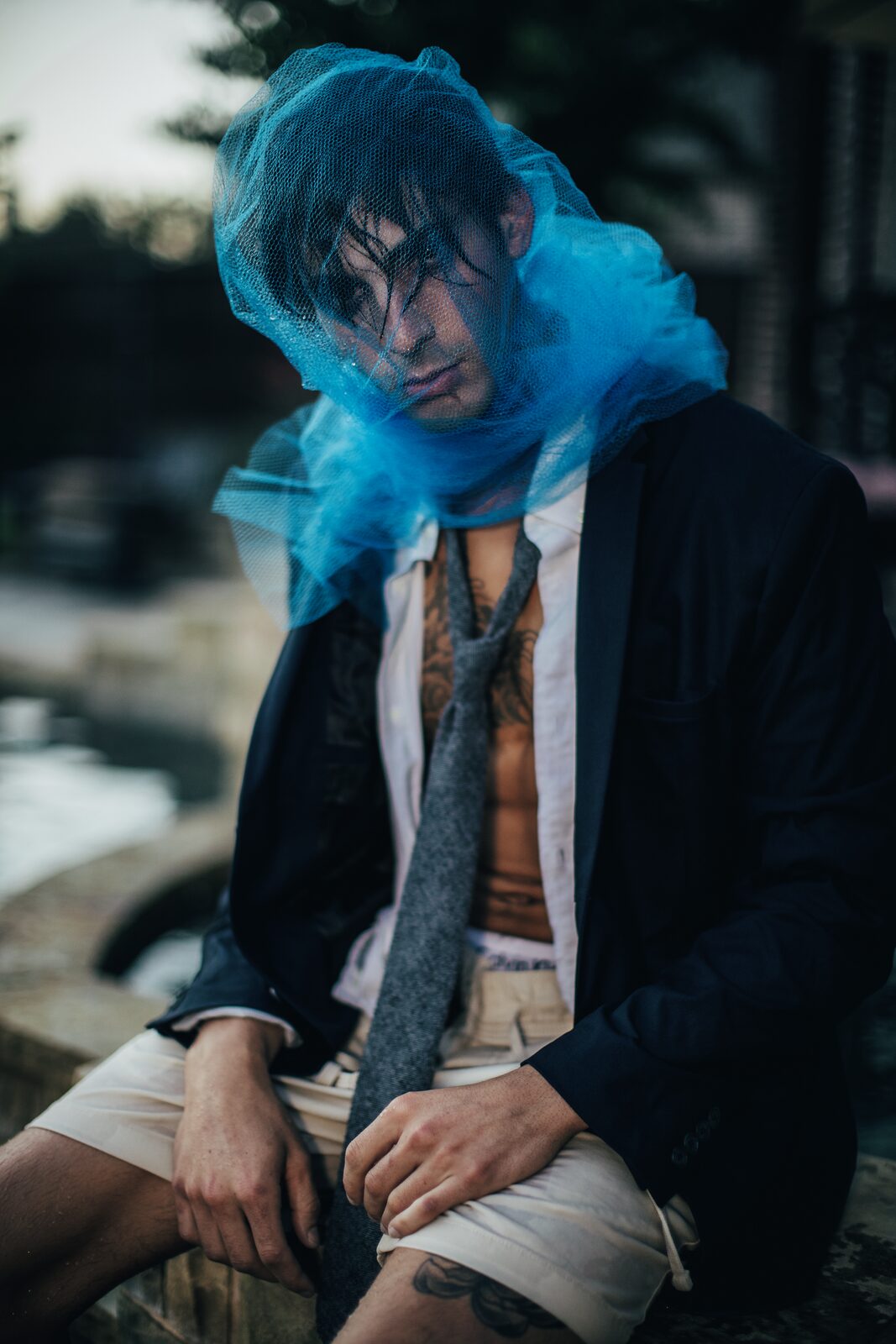 Editorial fashion portrait, male model with blue tulle veil and tattoos, photographed by Tony Liam