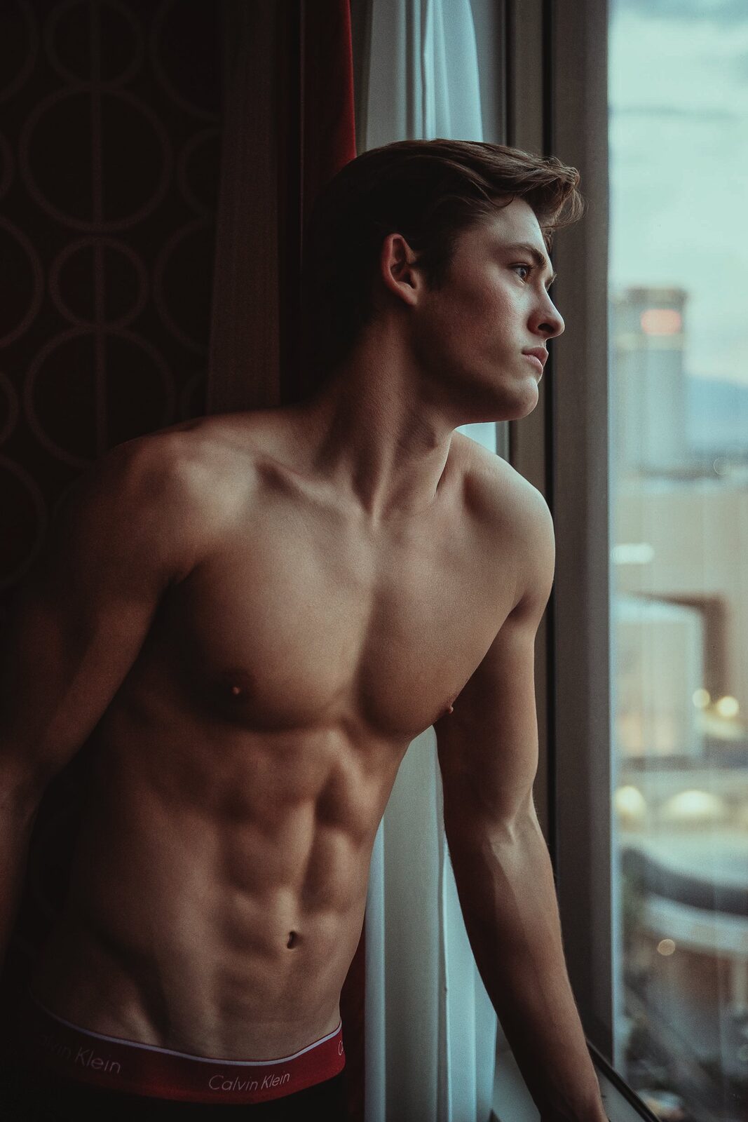 Male model in profile by hotel window at dusk, atmospheric portrait by Tony Liam