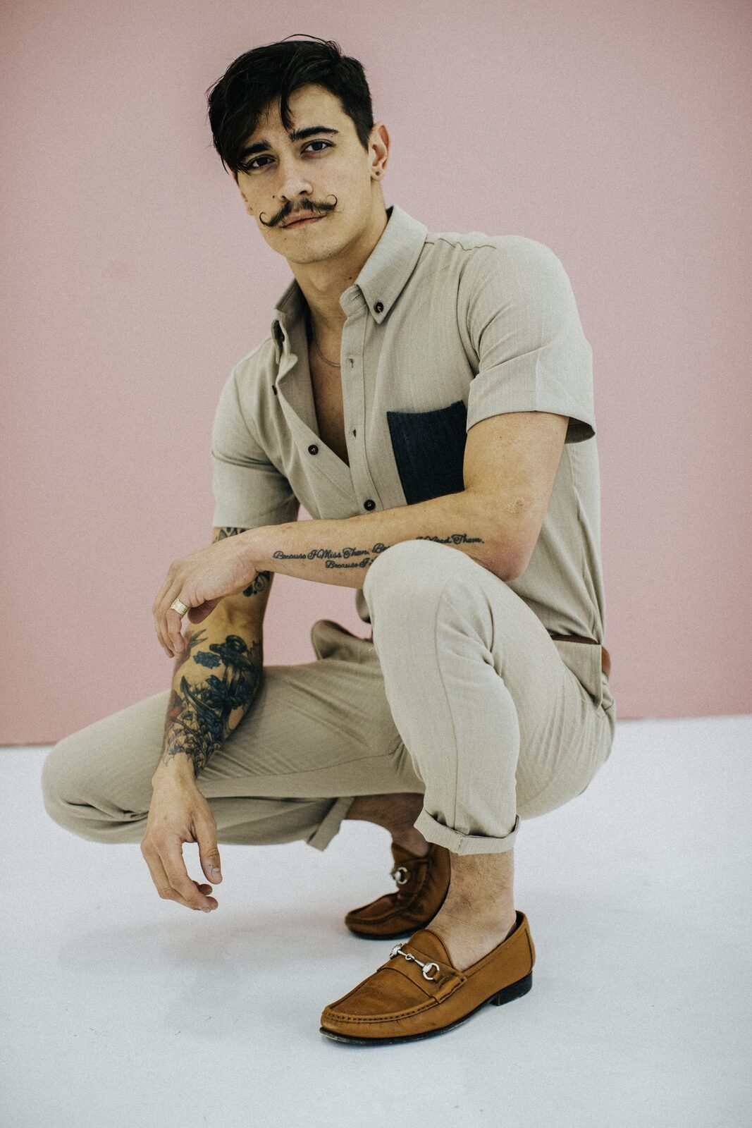 Male model crouched against pink studio backdrop in cream linen and Gucci loafers, campaign portrait by Tony Liam