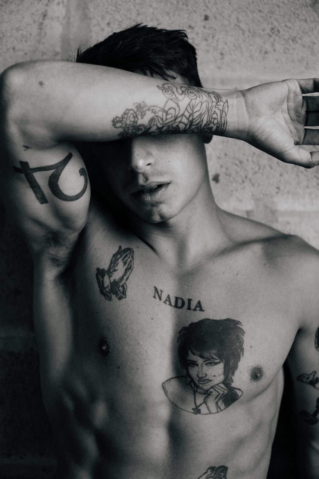 Black and white portrait of tattooed male model with arm across forehead, by Tony Liam